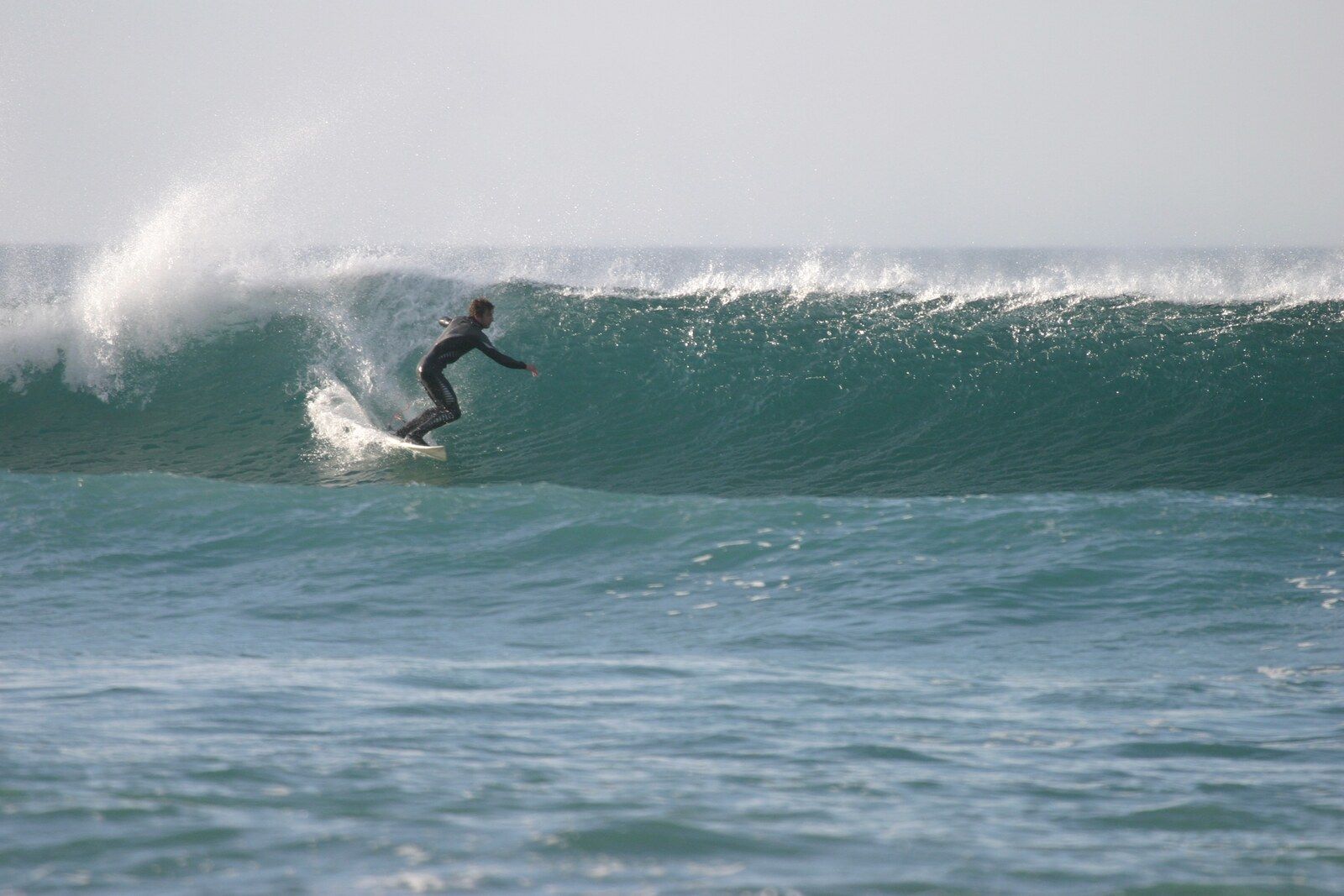 A surfer setting a line across a clean green wave at Chapel Porth