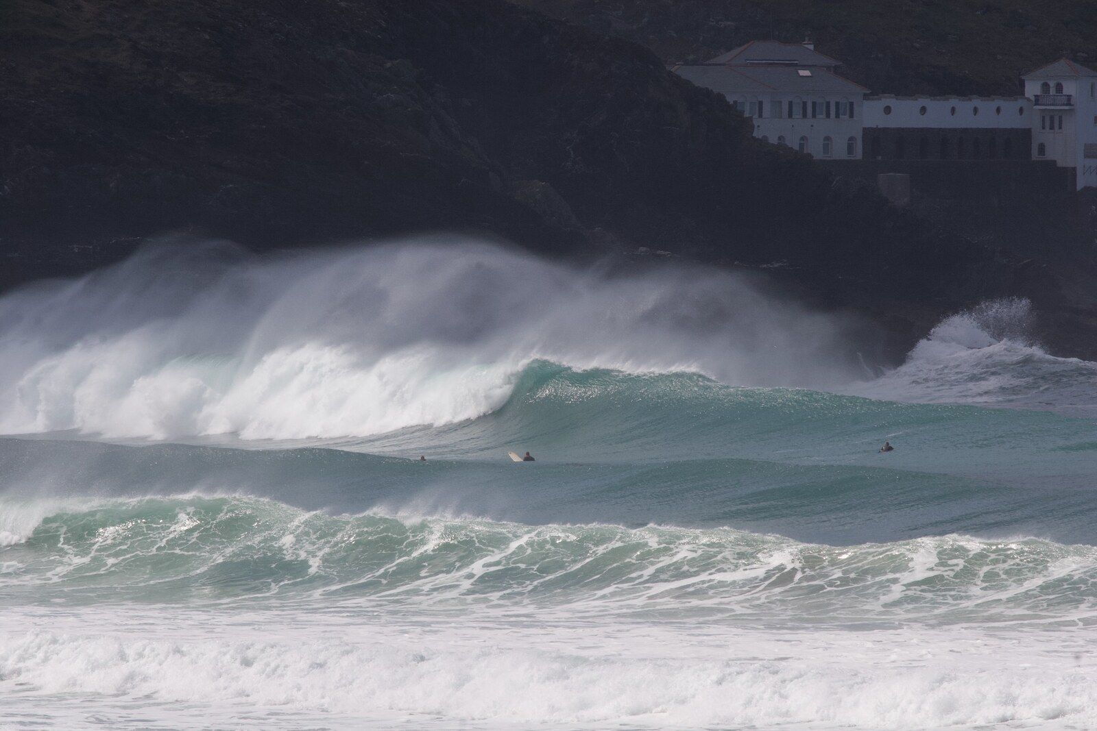 Large turquoise waves breaking at Fistral with surfers below the Headland Hotel