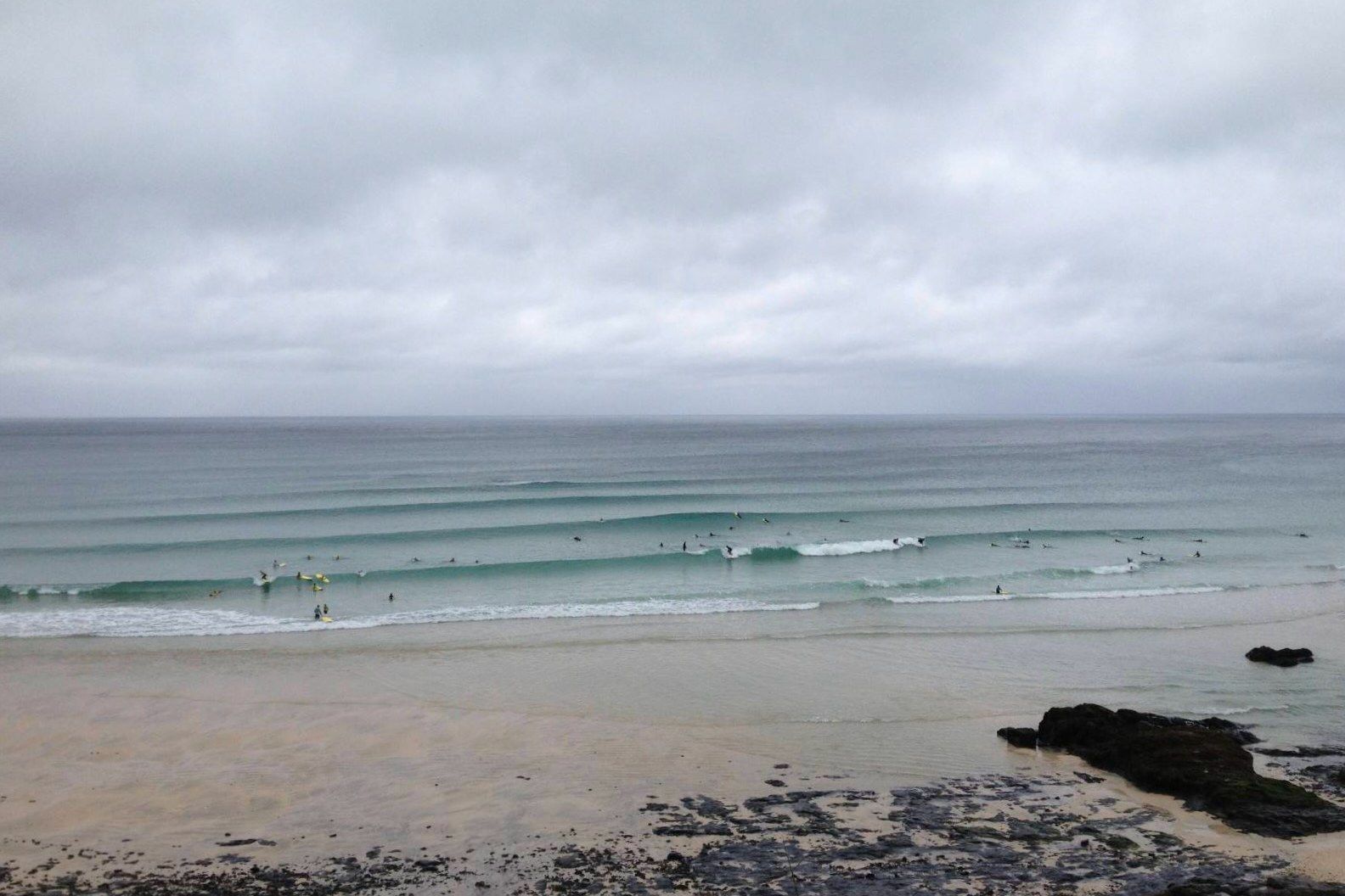 Lines of small clean surf with surfers spread across Porthmeor beach