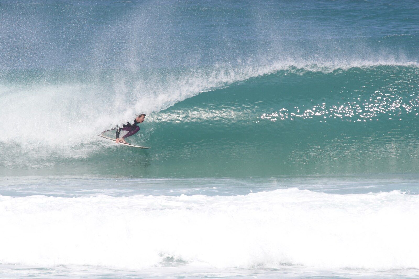 A surfer tucked under the turquoise lip of a breaking wave at Porthtowan