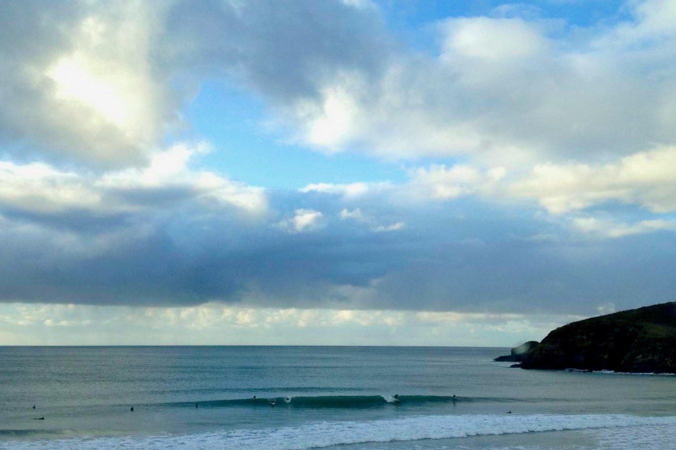 Surfers sharing a clean winter wave at Praa Sands with the rocky headland beyond